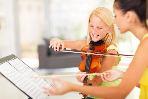 Girl plays violin aside teacher