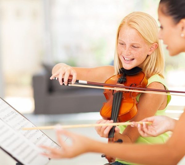 Girl plays violin aside teacher