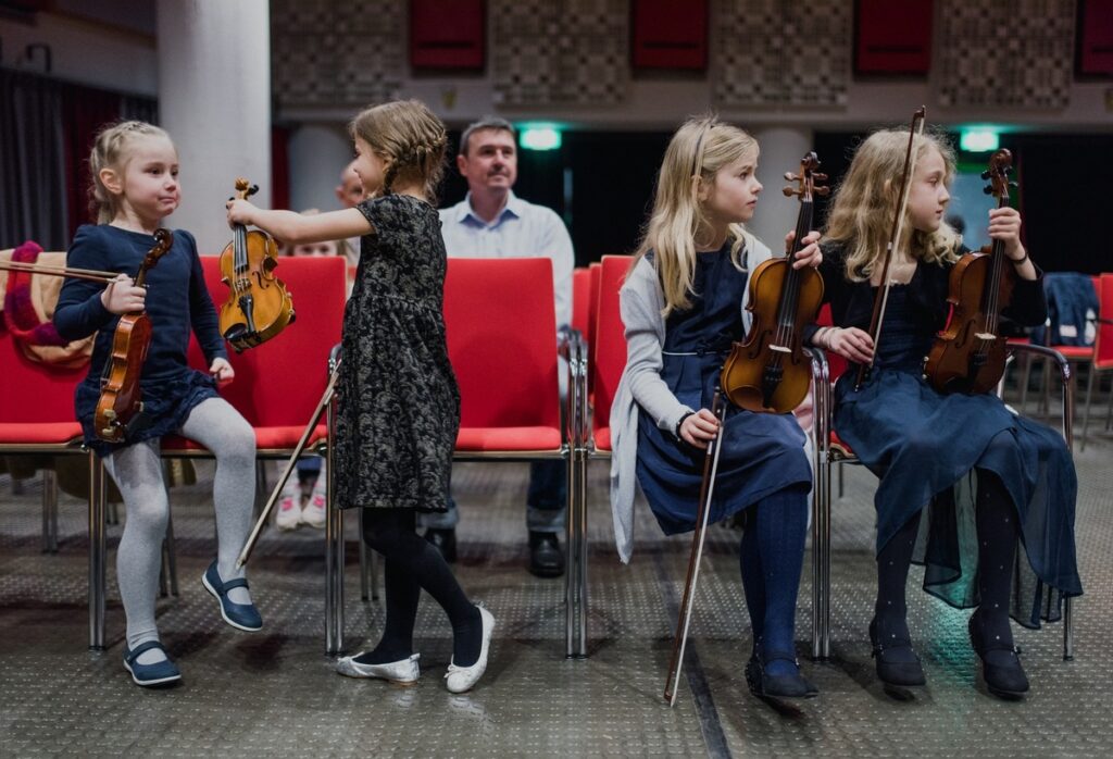 Vier Geigenschülerinnen in eleganten Kleidern halten jede ihre Geige
