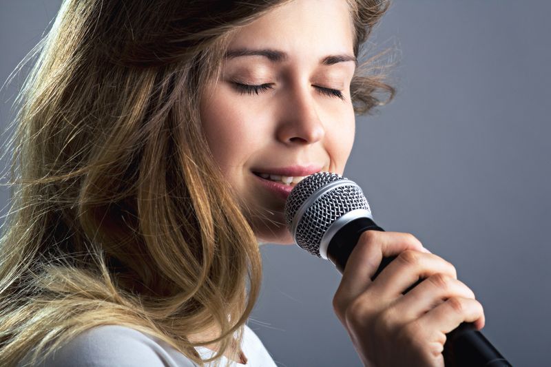 Blonde Gesangsschülerin singt in Mikrofon bei Gesangsunterricht
