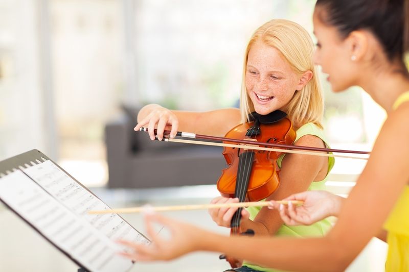 Geigenschülerin spielt Geige mit Geigenlehrerin vor Notenblättern