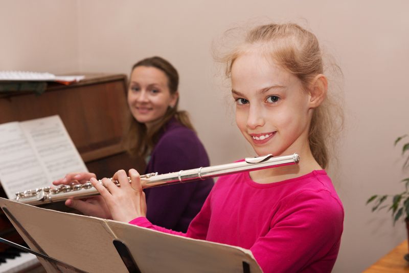 Blonde Musikschülerin lernt Querflöte mit Musiklehrerin am Klavier