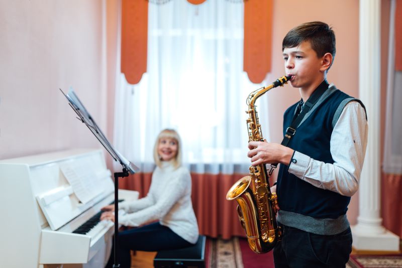 Ein Junge spielt Saxophon mit Musiklehrerin am Klavier